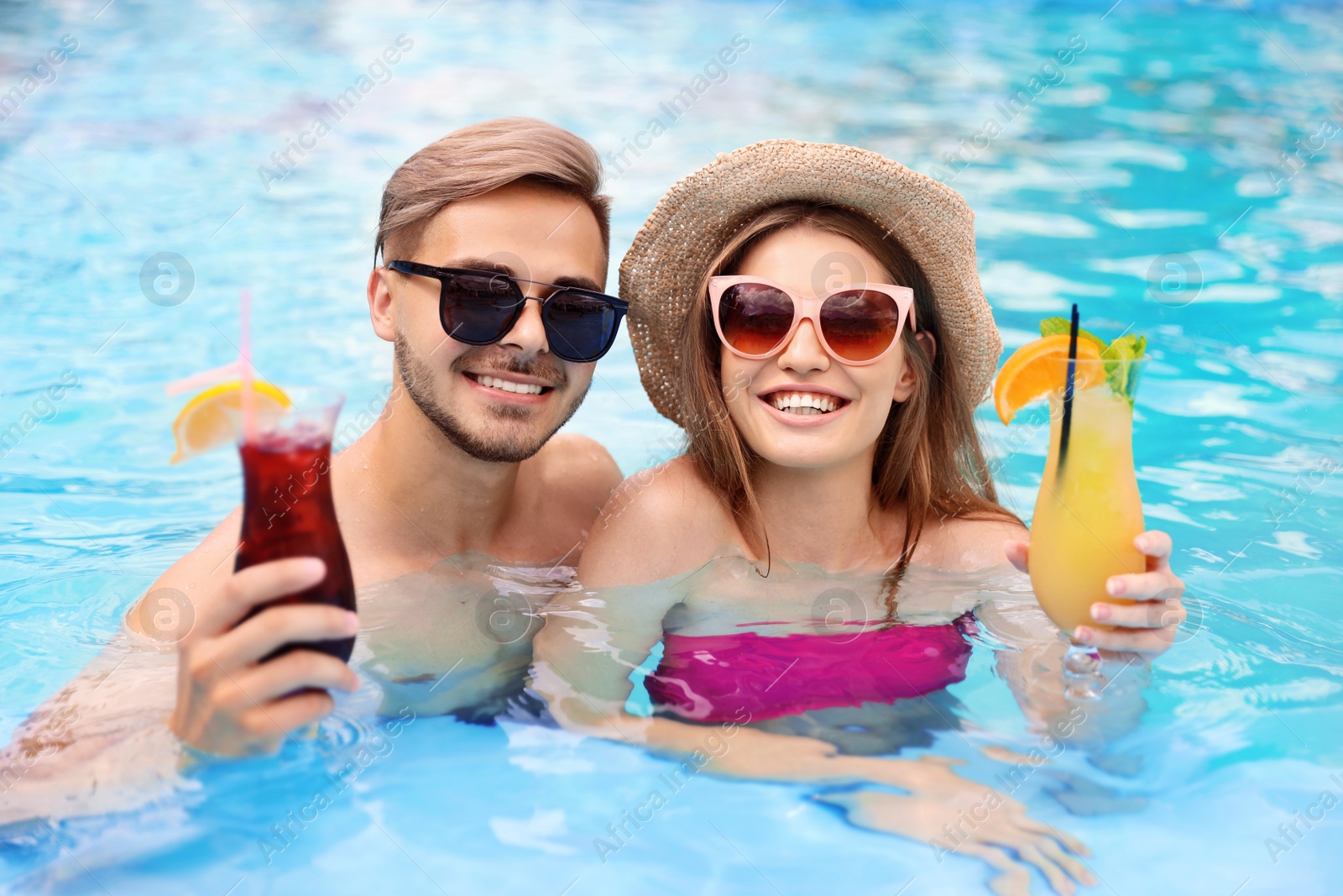 Photo of Young couple with cocktails in pool on sunny day