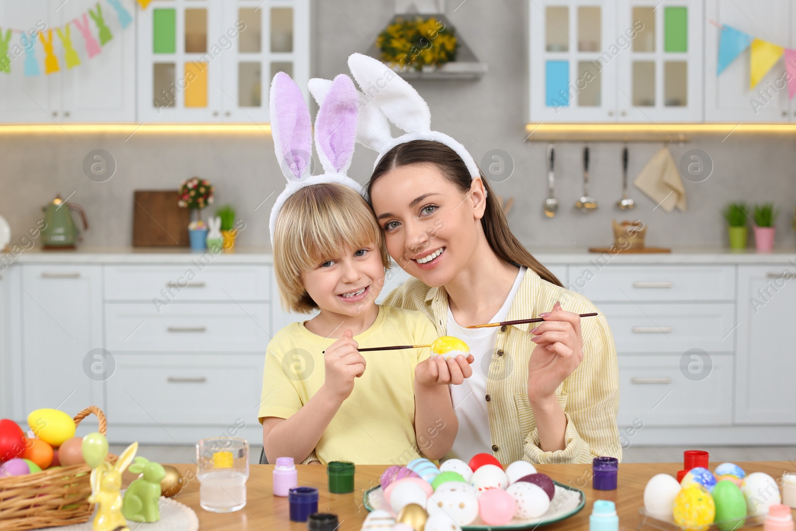 Photo of Mother and her cute son painting Easter eggs at table in kitchen