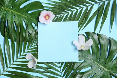 Photo of Flat lay composition with tropical leaves and Hibiscus flowers on blue background. Space for text