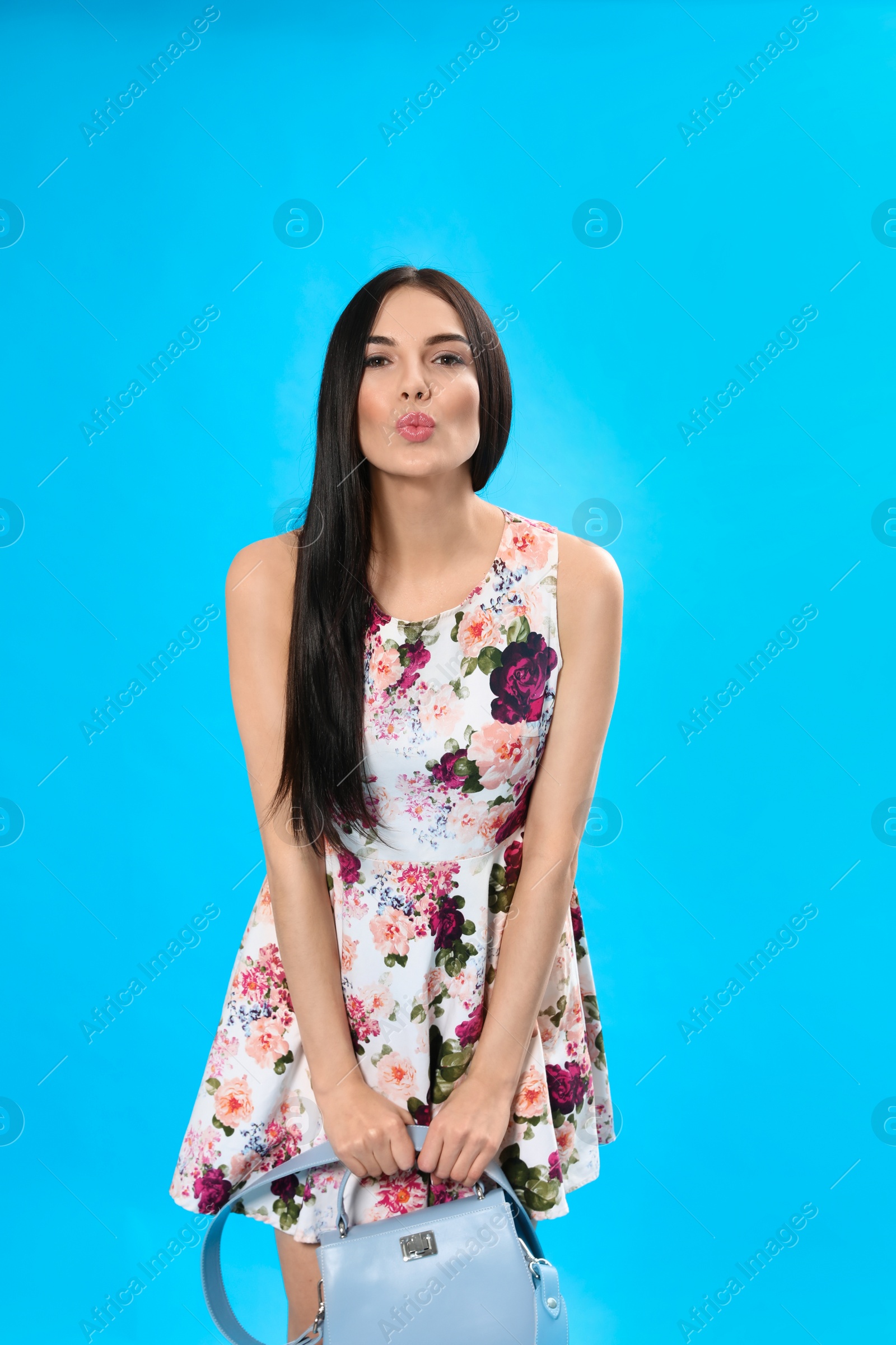 Photo of Young woman wearing floral print dress with stylish handbag on light blue background