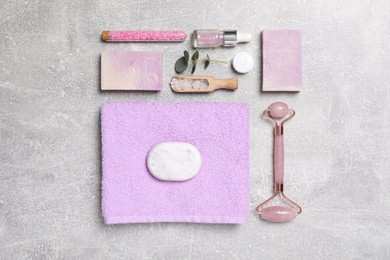 Photo of Flat lay composition with face roller and cosmetic products on light grey stone table