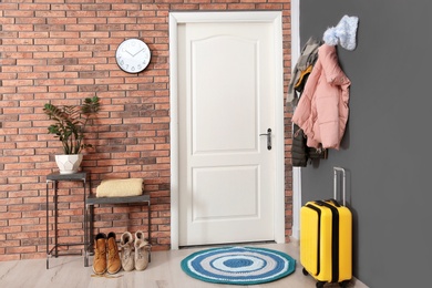 Photo of Modern hallway interior with stylish furniture, suitcase and clothes on wall