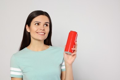 Photo of Beautiful young woman holding red tin can with beverage on light grey background. Space for text