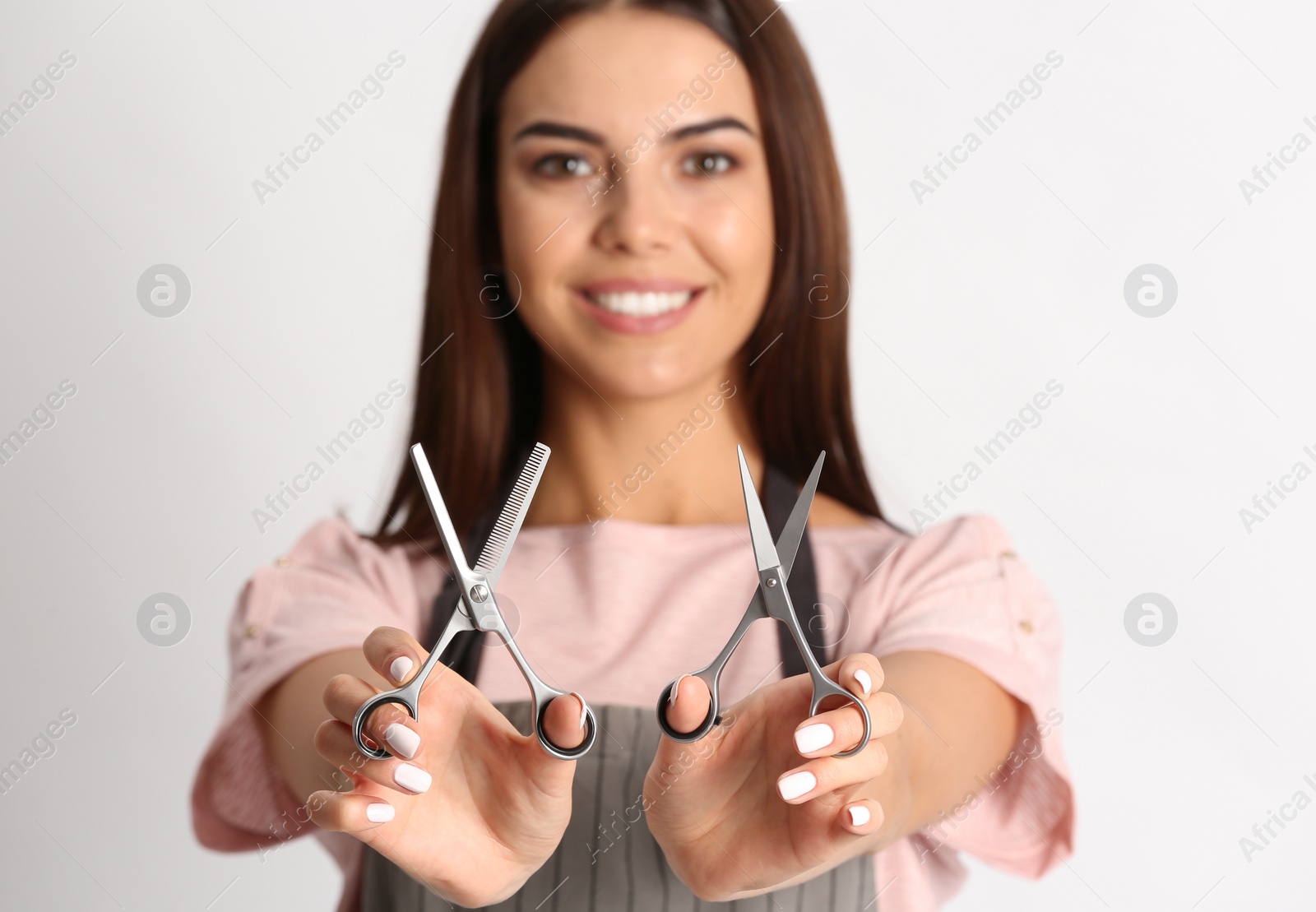 Photo of Young hairstylist holding professional scissors on light background, focus on hands