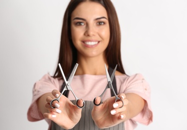 Photo of Young hairstylist holding professional scissors on light background, focus on hands