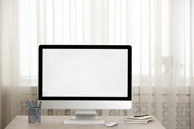 Modern computer with blank screen and stationery on table indoors. Space for design