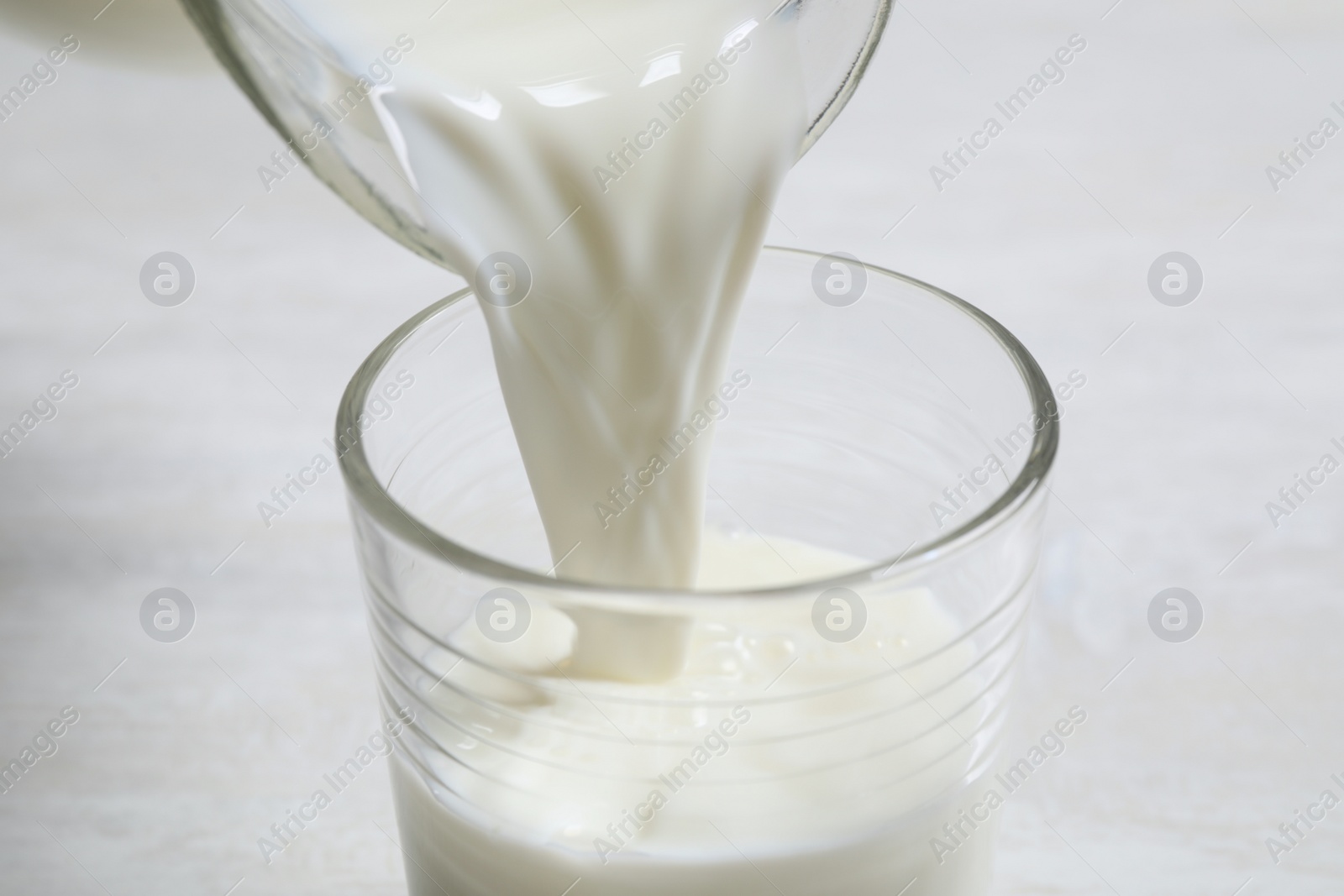 Photo of Pouring milk into glass on white table, closeup