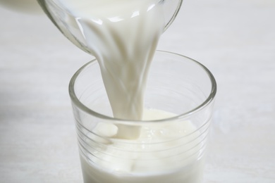 Pouring milk into glass on white table, closeup