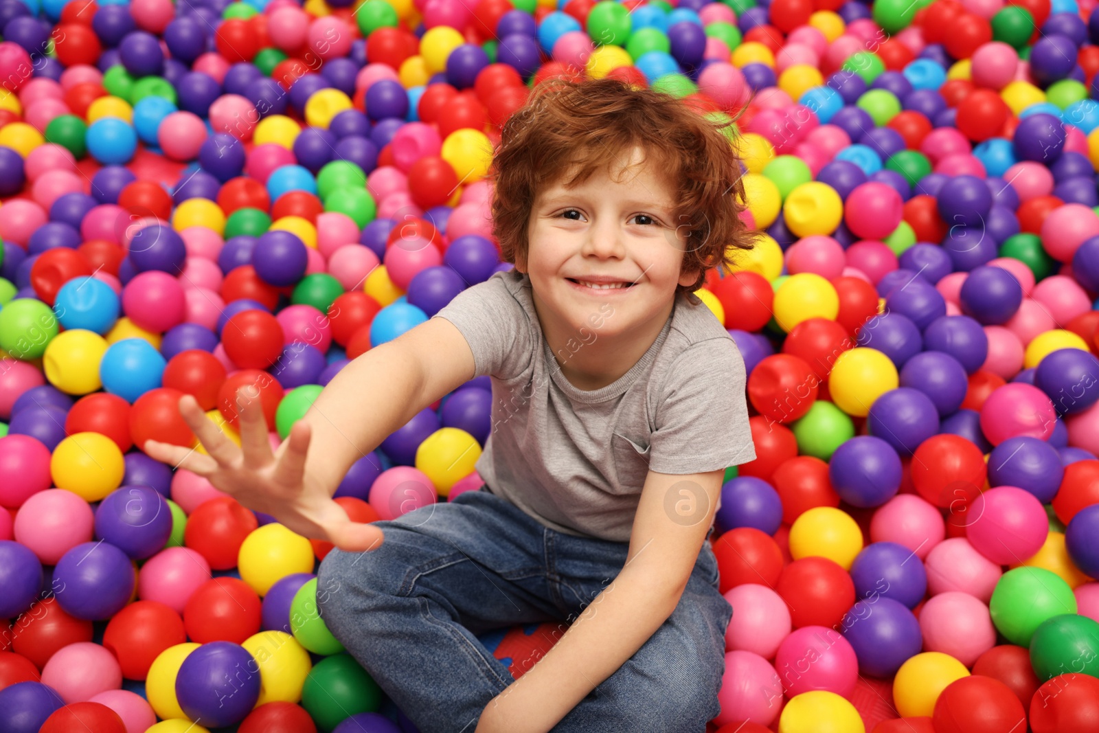 Photo of Happy little boy sitting on colorful balls in ball pit