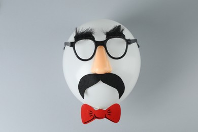 Photo of Man's face made of balloon, funny mask with fake mustache, nose and glasses on grey background, top view