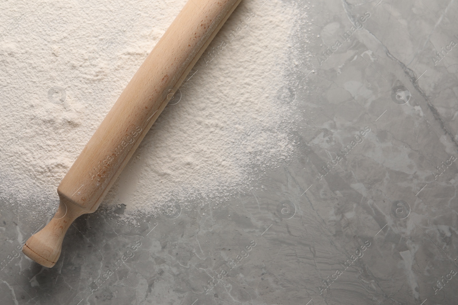 Photo of Pile of flour and rolling pin on grey marble table, top view. Space for text