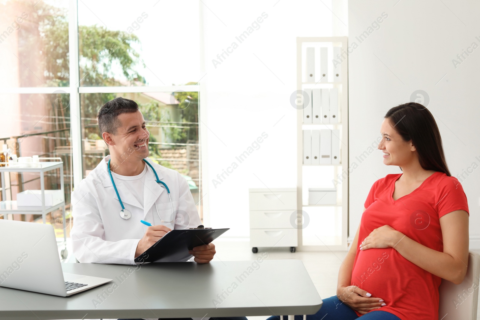 Photo of Young doctor with pregnant woman in hospital. Patient consultation