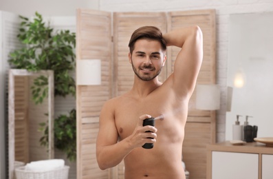 Handsome young man applying deodorant in bathroom