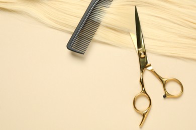 Photo of Professional scissors and comb with blonde hair strand on beige background, top view. Space for text