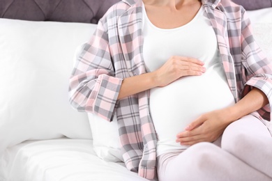 Happy pregnant woman lying in bed at home, closeup