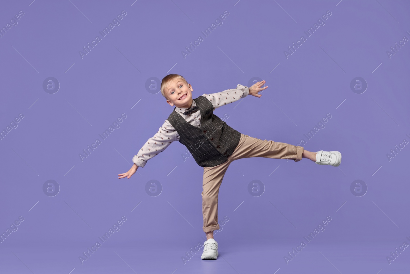 Photo of Happy little boy dancing on violet background. Space for text