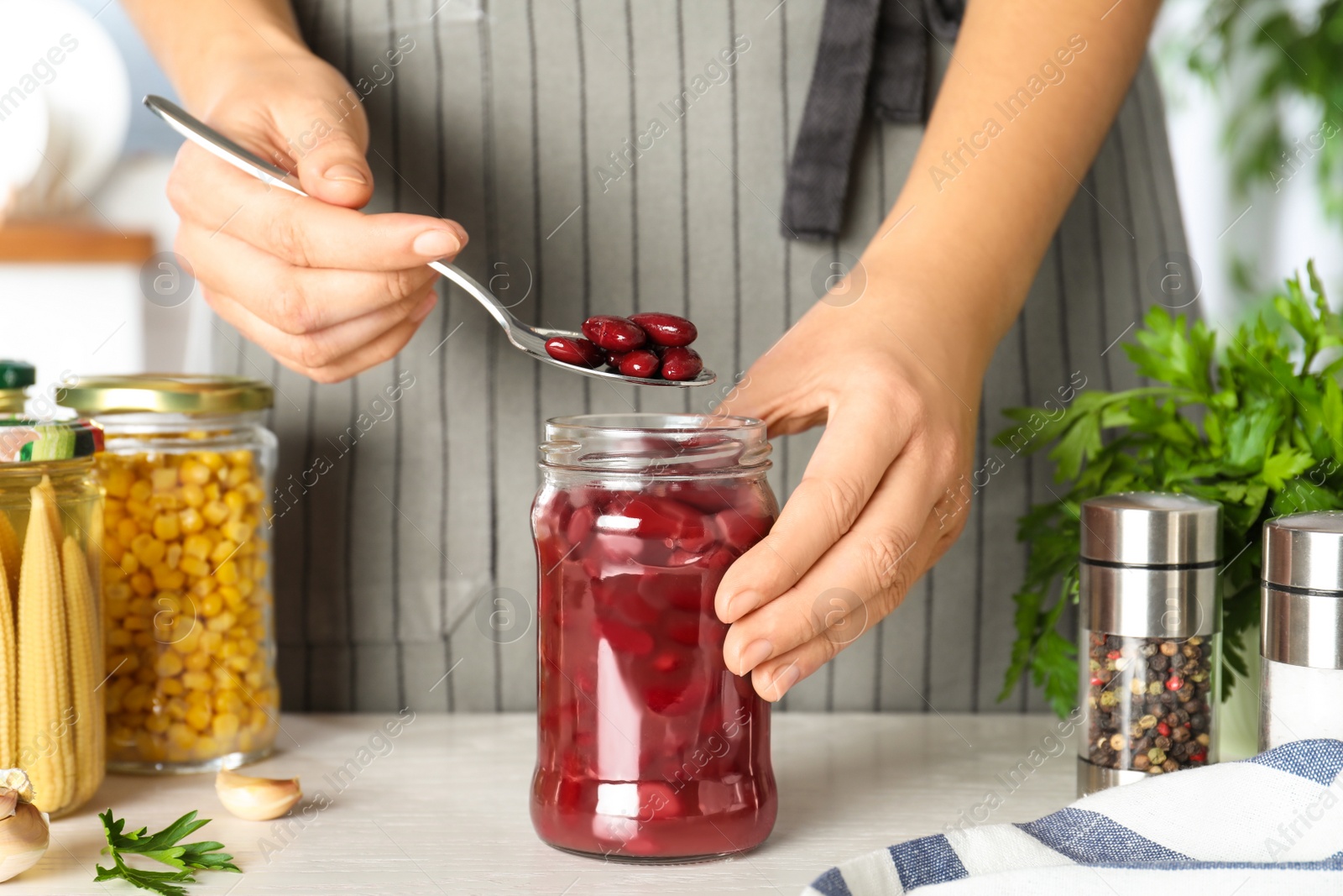 Photo of Woman putting beans into jar at white table, closeup