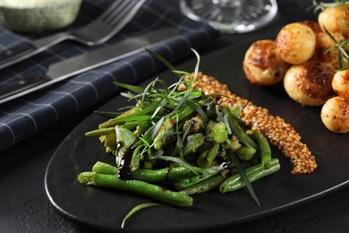 Photo of Delicious salad with tarragon, mustard and grilled potatoes served on black table, closeup