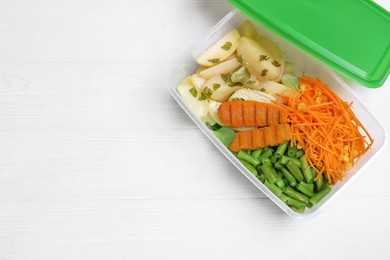 Tasty potatoes with cutlets and vegetables in plastic container on white wooden table, top view. Space for text