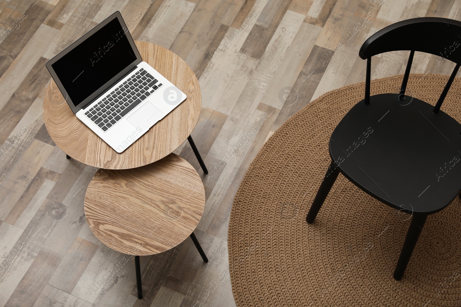 Photo of Modern laptop on wooden nesting table near black chair indoors, above view