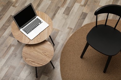 Photo of Modern laptop on wooden nesting table near black chair indoors, above view