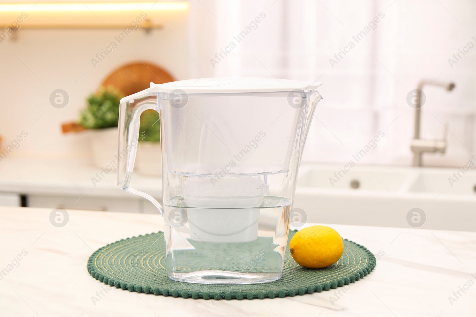 Photo of Water filter jug and lemon on white marble table in kitchen