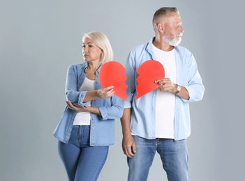 Photo of Mature couple with torn paper heart on grey background. Relationship problems