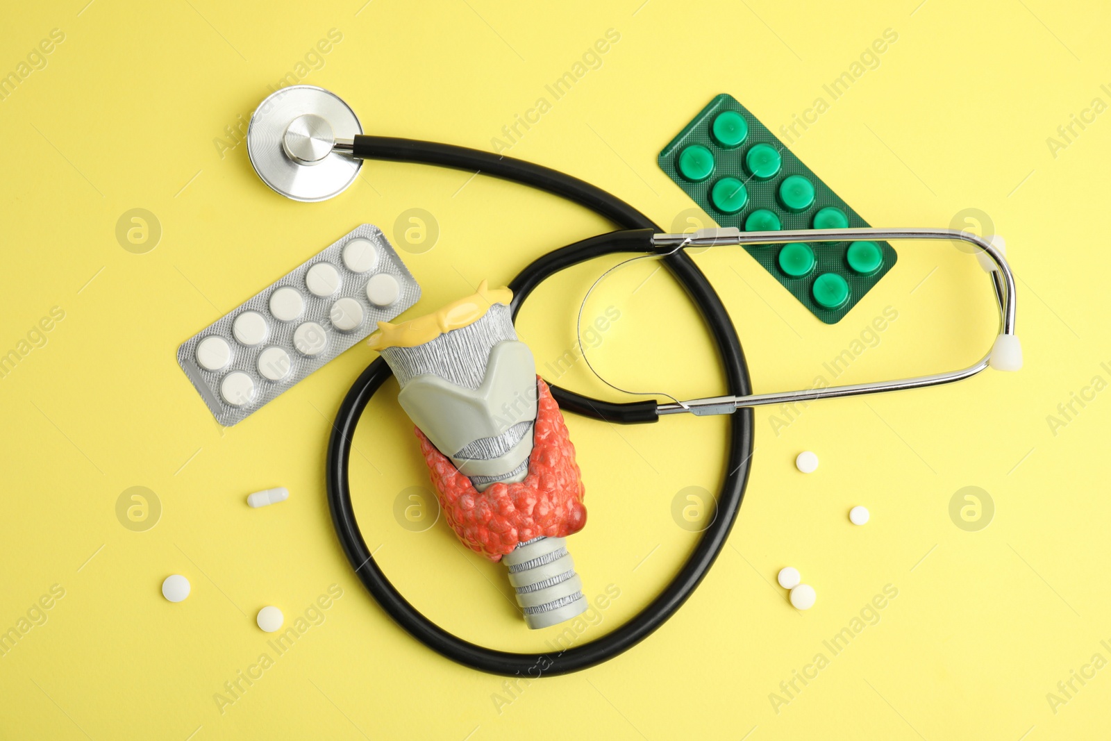 Photo of Plastic model of thyroid with tumor, pills and stethoscope on yellow background, flat lay