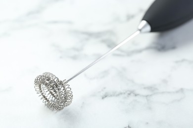 Photo of Black milk frother wand on white marble table, closeup