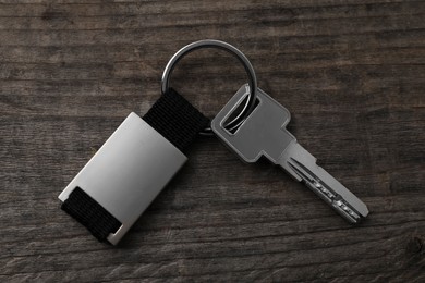 Key with metallic keychain on wooden background, top view