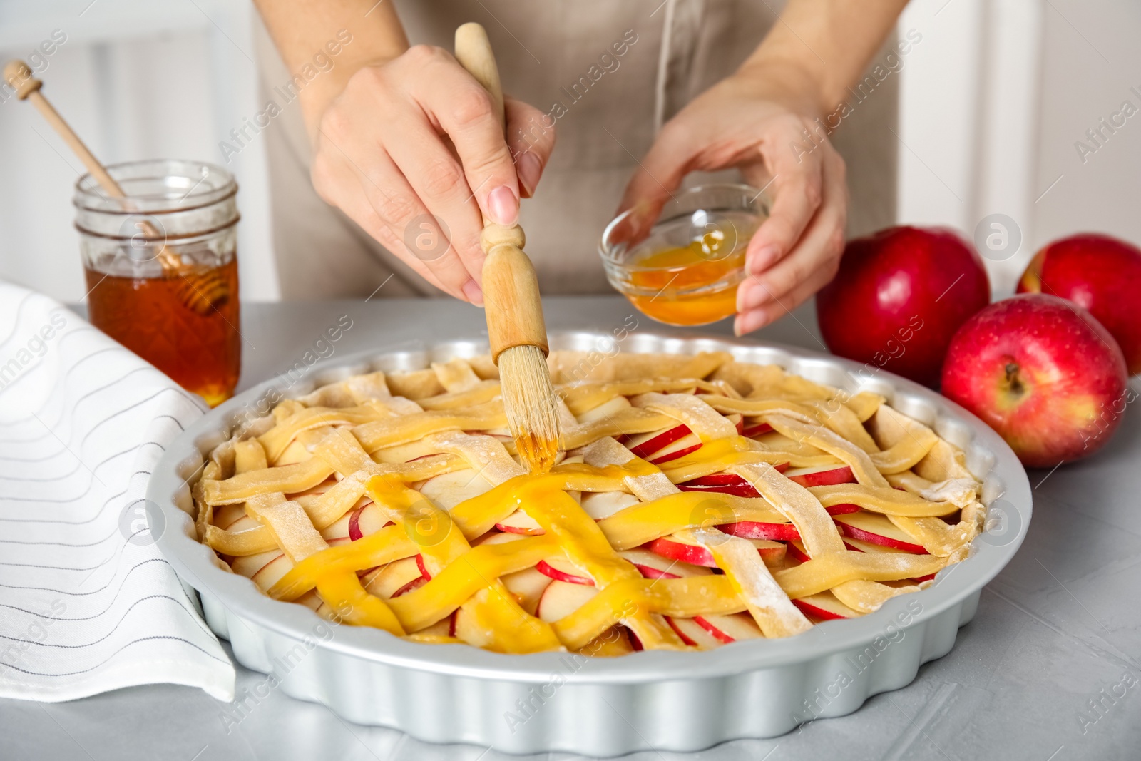 Photo of Woman applying liquid egg onto traditional English apple pie with brush at light grey table, closeup