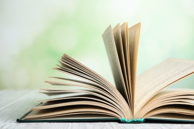 Photo of Open book on white wooden table against blurred green background, closeup