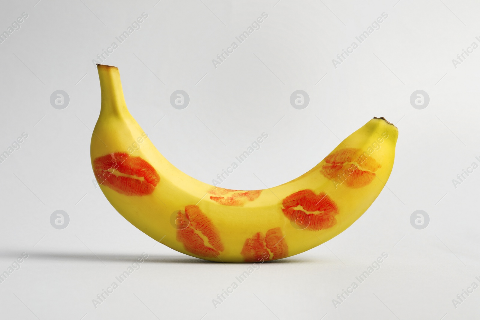 Photo of Banana covered with red lipstick marks on light grey background. Potency concept