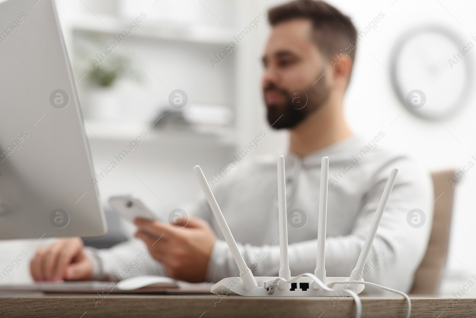 Photo of Man with computer and smartphone working at wooden table, focus on Wi-Fi router