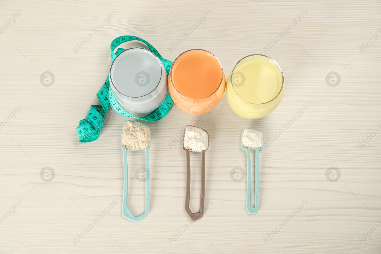 Photo of Tasty shakes, scoops with different powders and measuring tape on light wooden table, flat lay. Weight loss