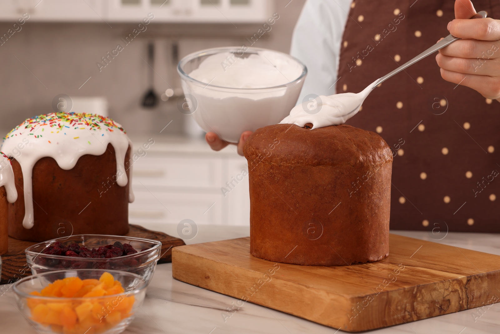 Photo of Woman decorating traditional Easter cake with glaze at white marble table in kitchen, closeup