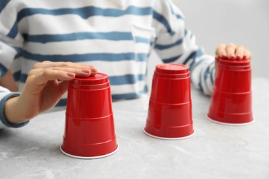 Photo of Woman playing shell game with red cups at light marble table, closeup