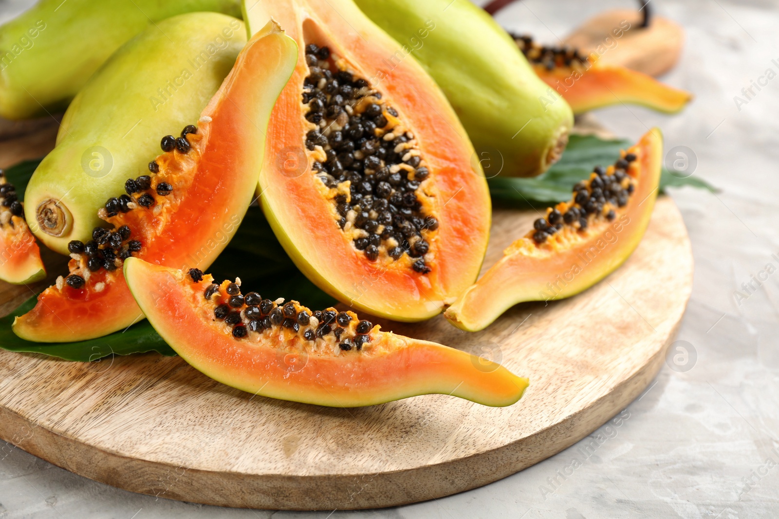 Photo of Fresh ripe papaya fruits with green leaves on grey table, closeup