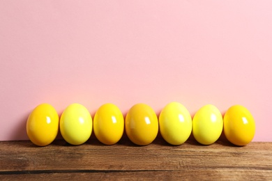 Easter eggs on wooden table against pink background, space for text