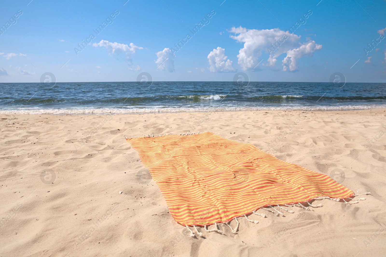 Photo of Orange striped beach towel on sandy seashore
