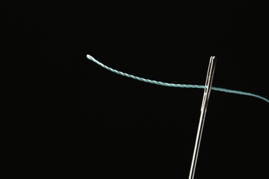 Photo of Needle with sewing thread on black background, closeup