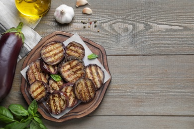 Photo of Delicious grilled eggplant slices served on wooden table, flat lay. Space for text