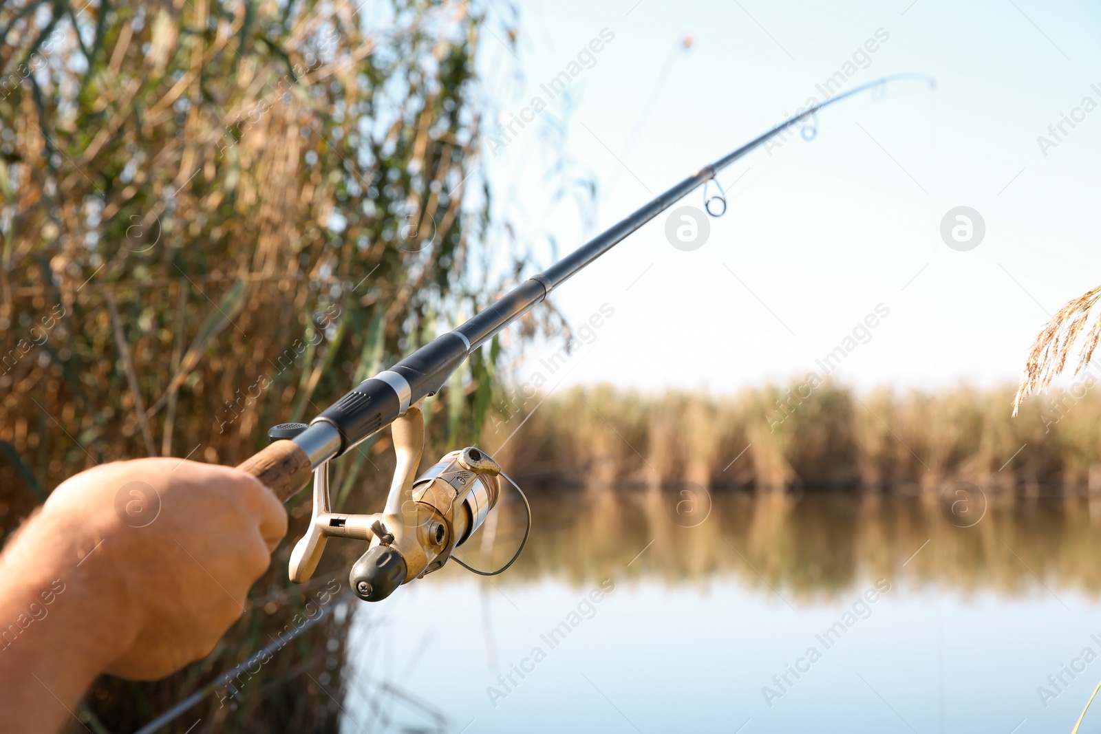 Photo of Man fishing alone at riverside on sunny day, closeup