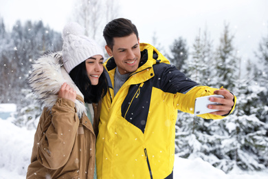 Photo of Happy couple taking selfie near snowy forest. Winter vacation