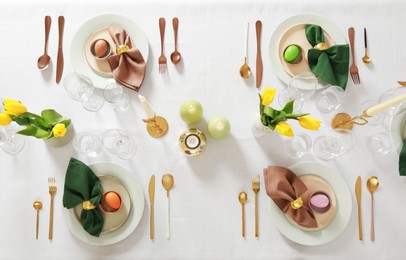 Festive Easter table setting with painted eggs, burning candles and yellow tulips, flat lay