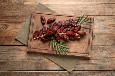 Photo of Sweet dried dates with green leaves on wooden table, top view