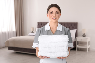 Image of Beautiful chambermaid with clean folded towels near bed in hotel room