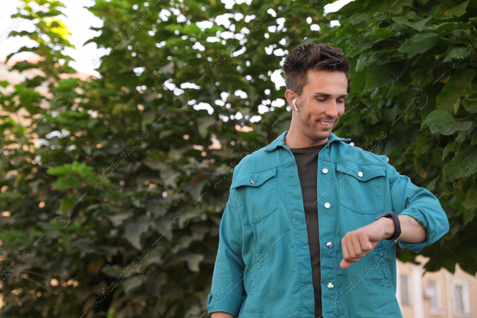 Photo of Young man with wireless earphones and smart watch in park