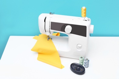 Photo of Modern sewing machine on table against color background