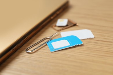 Photo of SIM cards, mobile phone and ejector tool on wooden table, closeup